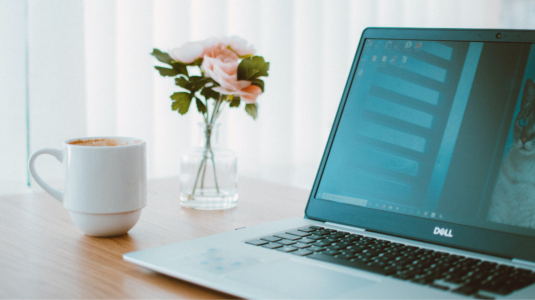 Laptop, vase of flowers and coffee mug on a desk