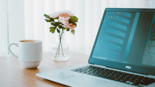 Laptop, vase of flowers and coffee mug on a desk
